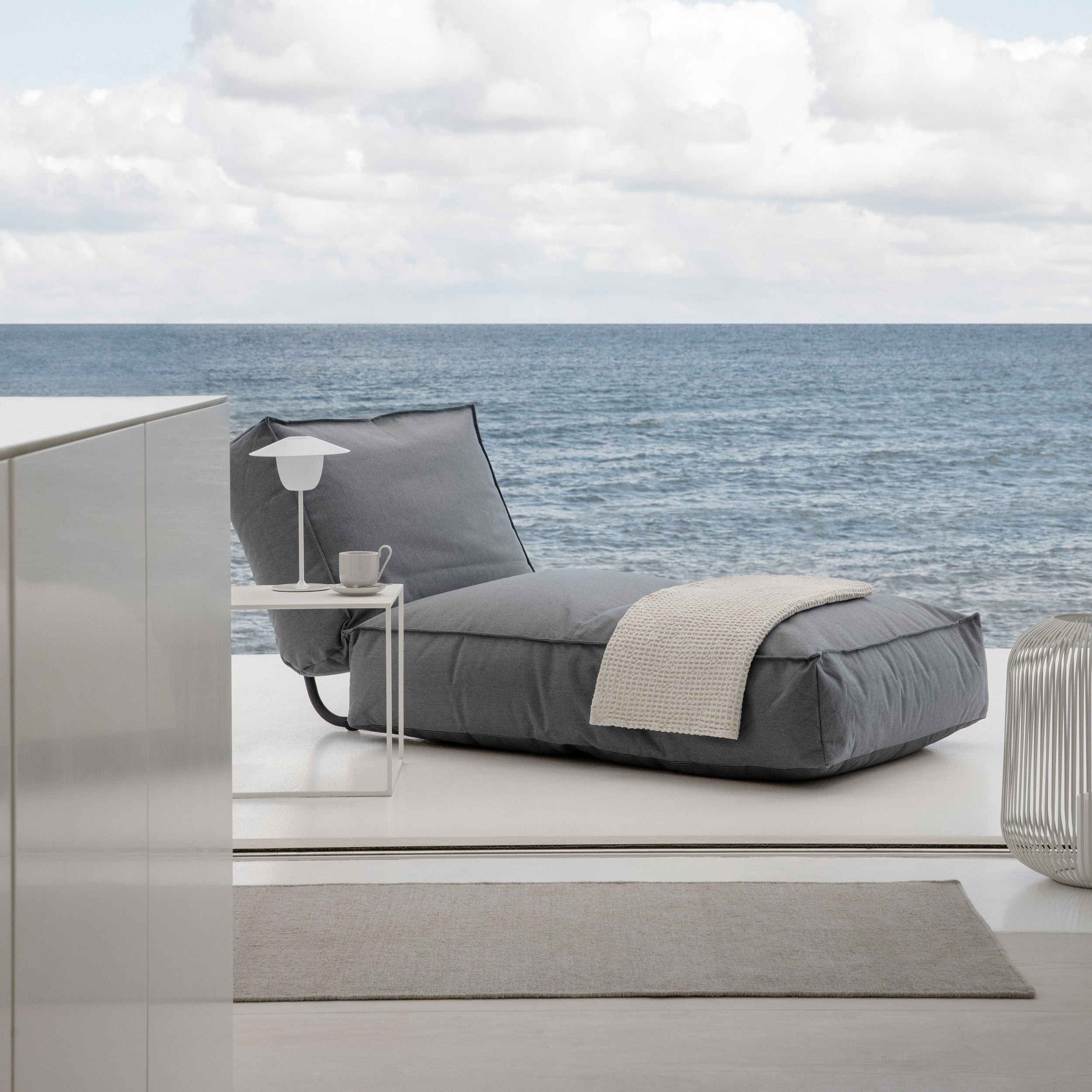 Gray lounge chair with a blanket on a modern patio with ocean view