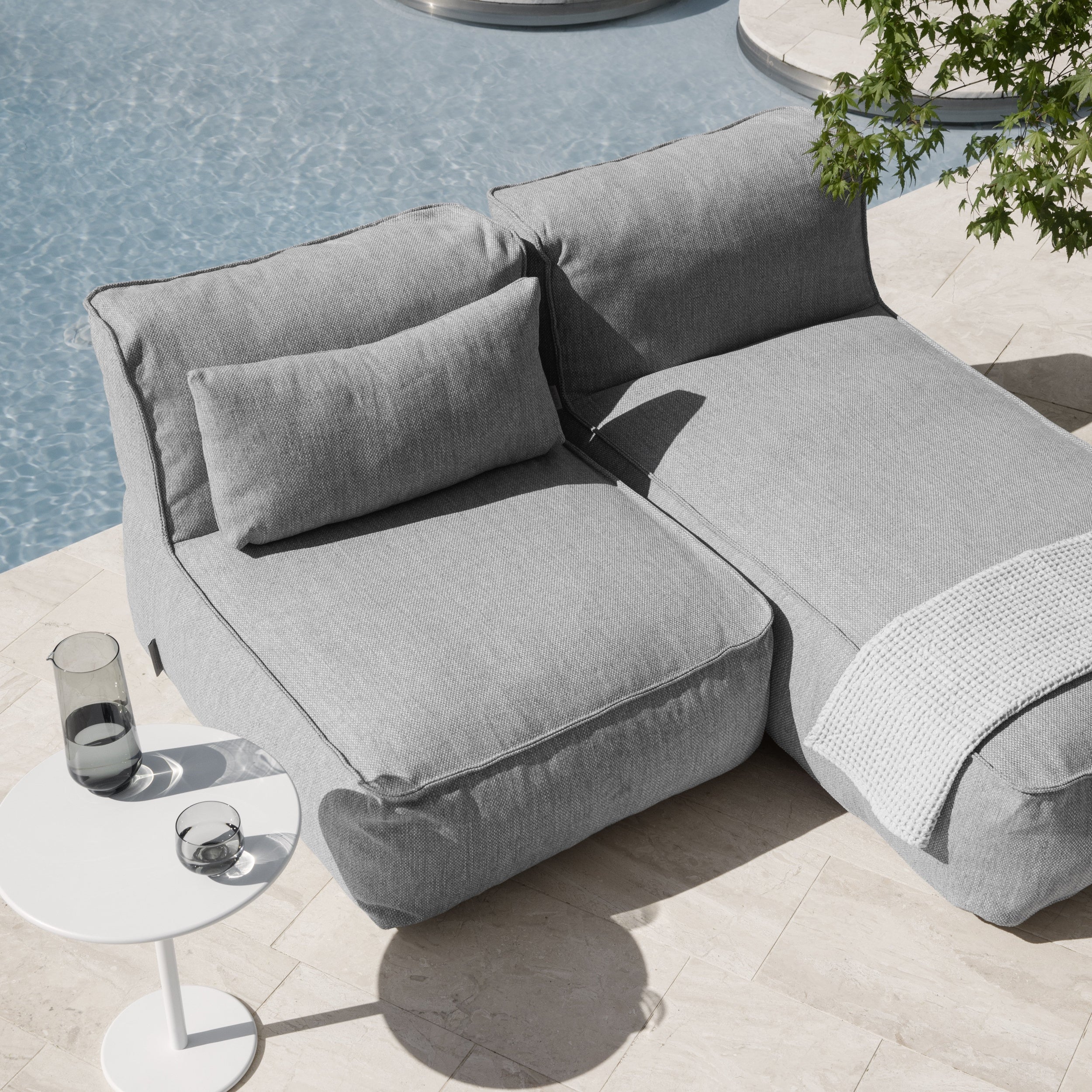 Gray outdoor sofa with cushions on a patio near a pool
