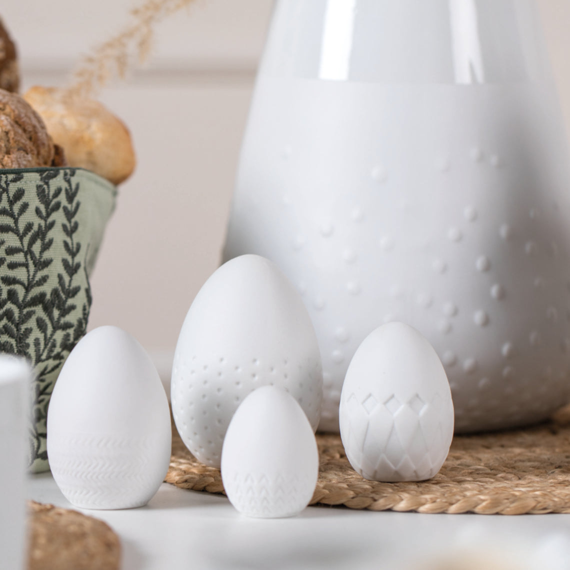 4 White Porcelain Easter Eggs on a counter with white porcelain vase in the background