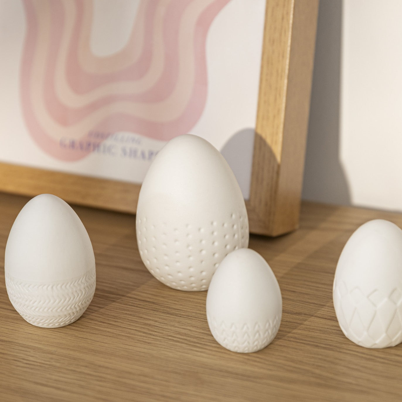 4 White Porcelain Easter Eggs on a wood counter with artwork in the background