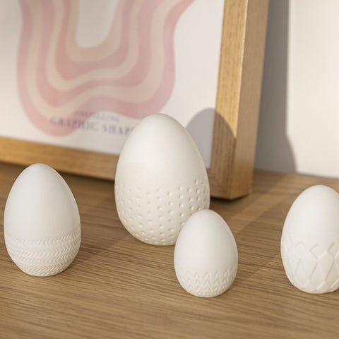 4 White Porcelain Easter Eggs on a wood counter with artwork in the background