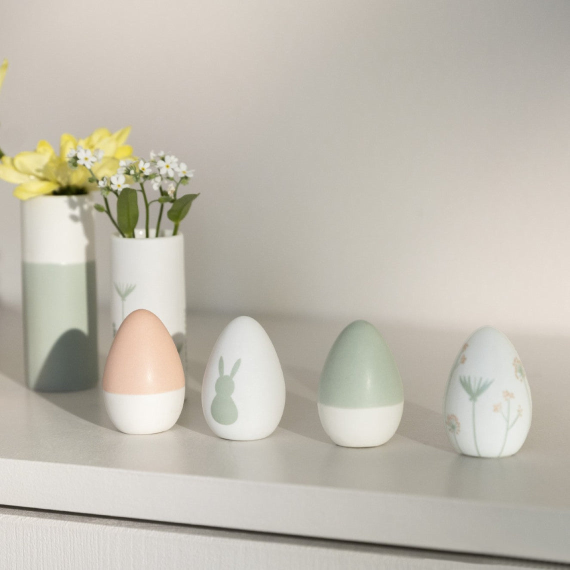 Four Porcelain Easter Eggs on a shelf with vases in the background.