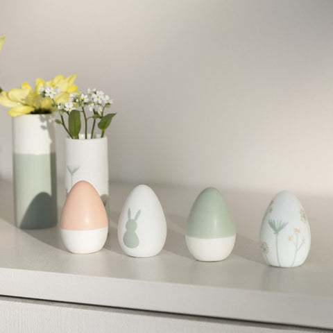 Four Porcelain Easter Eggs on a shelf with vases in the background.