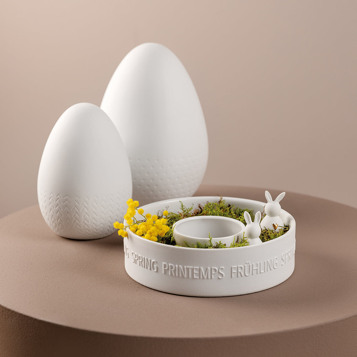 Two white porcelain bunnies in a container with decorative eggs in the background.