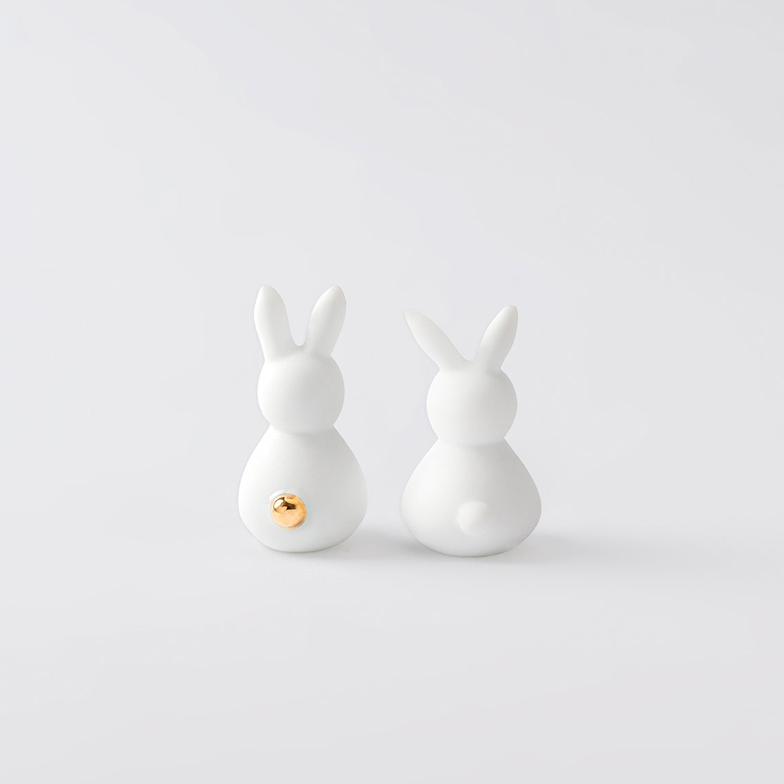 The back side of two porcelain bunnies showing their tails, on a white background.