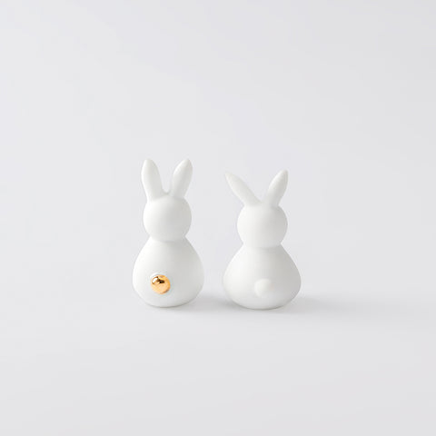 The back side of two porcelain bunnies showing their tails, on a white background.