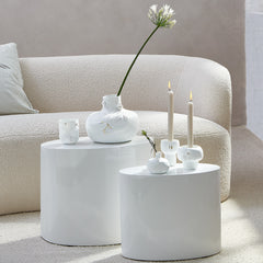 White porcelain vases and candle holders on a round white table with a beige sofa in the background.