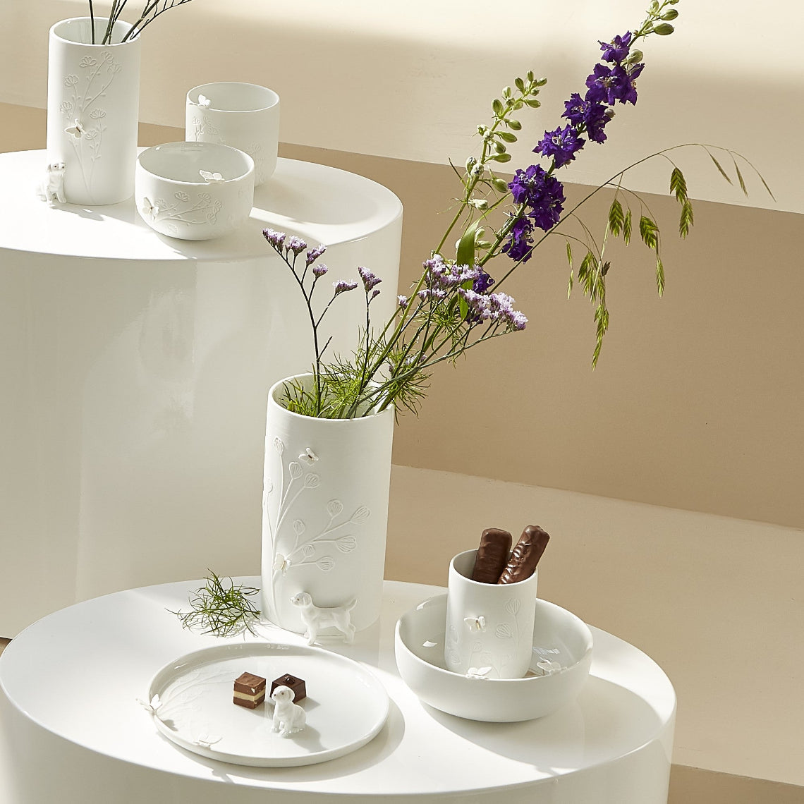 Porcelain Stories white porcelain items including cups, bowls, and a vase with flowers on a white surface.