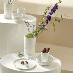 Porcelain Stories white porcelain items including cups, bowls, and a vase with flowers on a white surface.