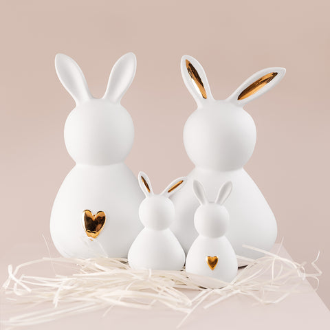 A set of four porcelain bunnies on a shelf with white straw around the bottom.